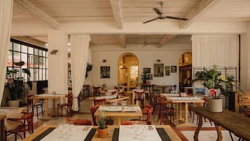 Un restaurante con mesas y sillas de madera, un ventilador de techo y plantas en macetas.