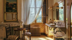 Une salle de bain avec un lavabo en marbre, une chaise en bois, un radiateur et une grande fenêtre avec des rideaux.