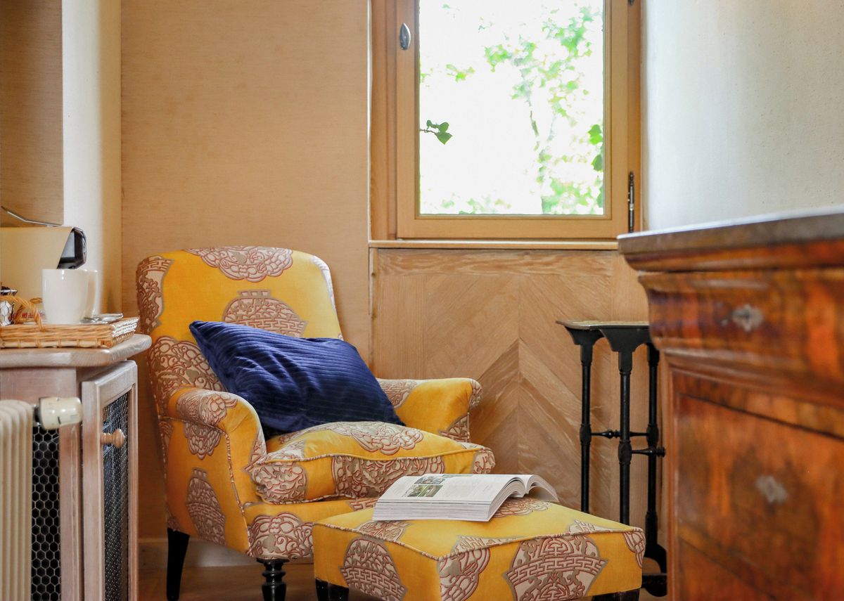 A room with a patterned armchair, a blue pillow, and a book on a small table.