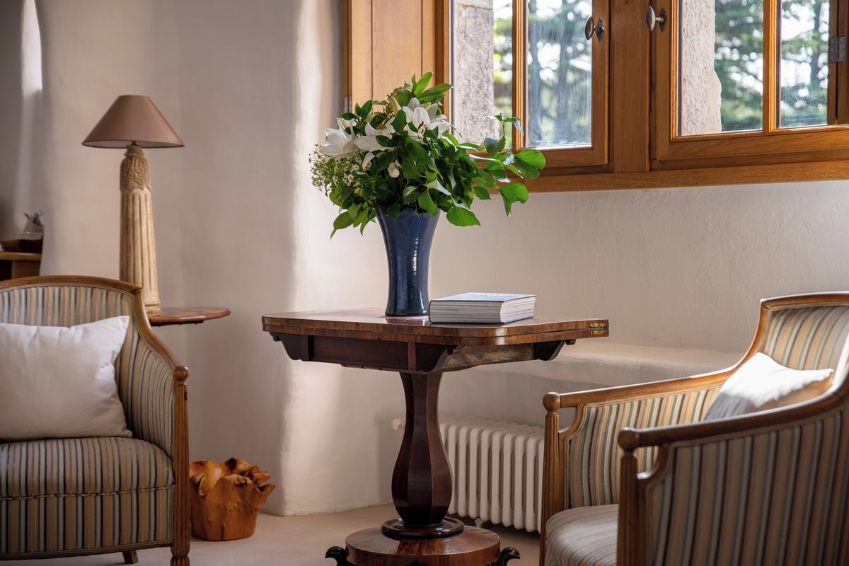 Una stanza con un tavolo rotondo in legno, un vaso blu con fiori, un libro e due poltrone imbottite.