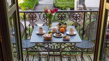 A balcony with a table set for breakfast, including cups, a teapot, fruits, and pastries.