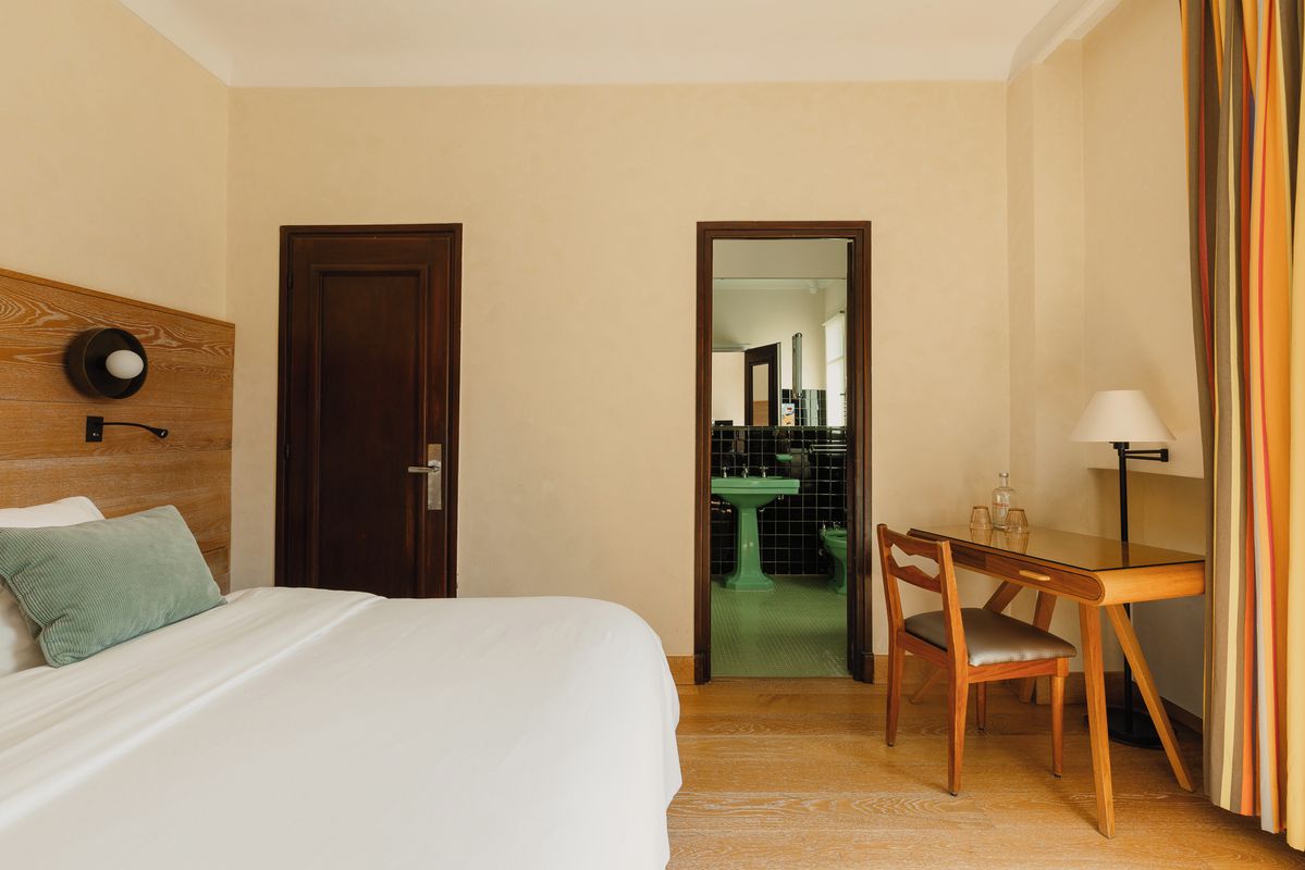 A hotel room with a bed, a desk, and a view into the bathroom.