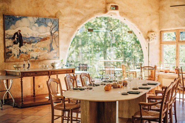 A dining area with a large table set for a meal, surrounded by wooden chairs, and a painting on the wall. - Le Grand Hôtel (Molitg-les-Bains)