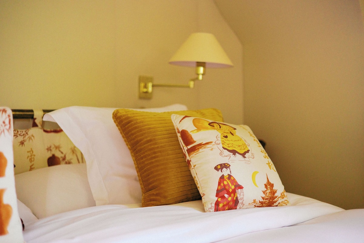 Una cama con ropa blanca y dos almohadones decorativos, uno con diseño tradicional y otro con estampado floral.