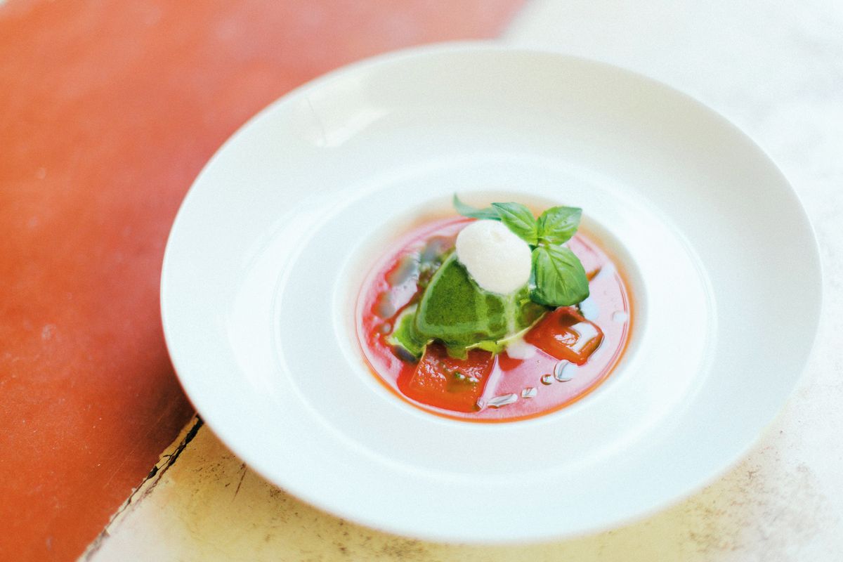 A white plate with a dessert consisting of a dollop of cream, a leaf of basil, and a red sauce.