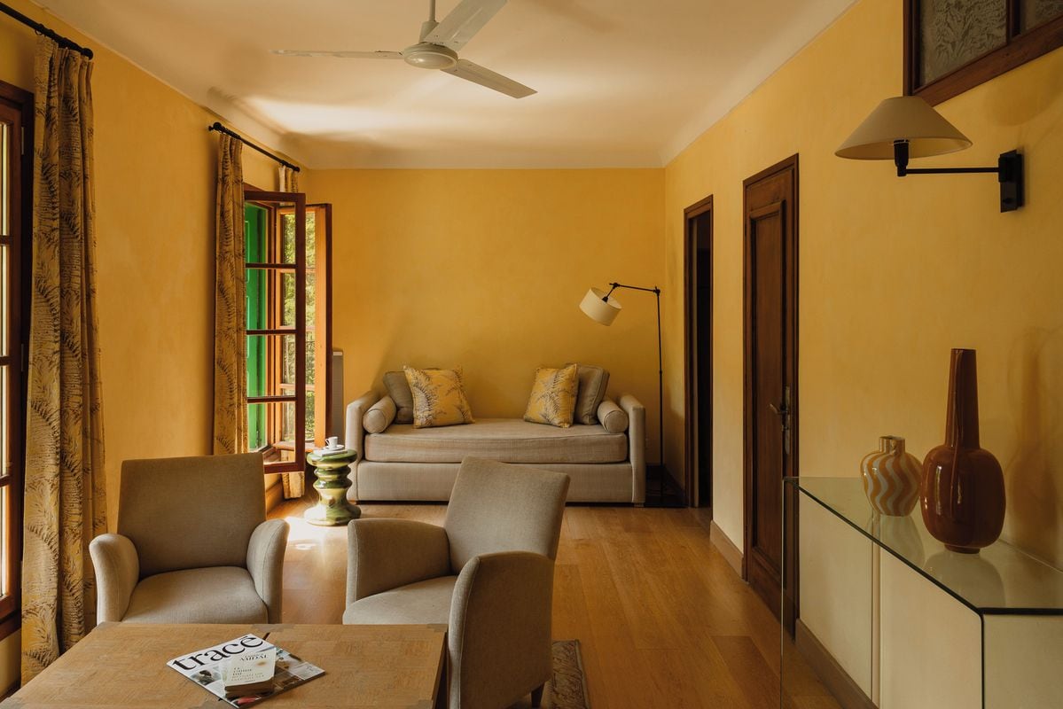 A room with a sofa, two armchairs, a table with a magazine, a floor lamp, and a ceiling fan.