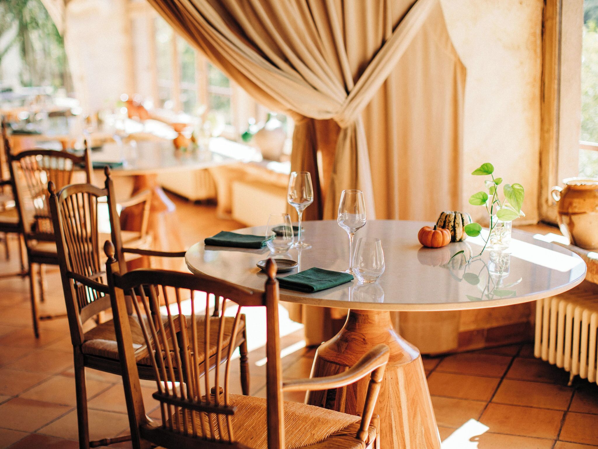 Un comedor con mesas redondas, sillas y copas de vino vacías.
