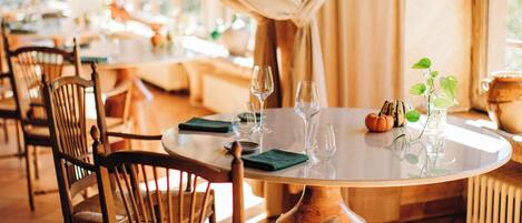 Un comedor con mesas redondas, sillas y copas de vino vacías.