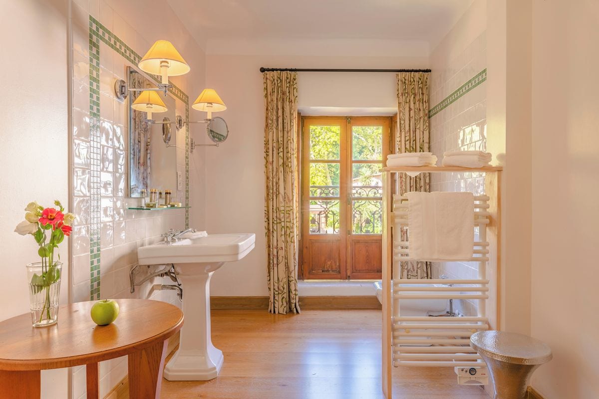 A bathroom with a pedestal sink, vanity mirror, and towel rack.