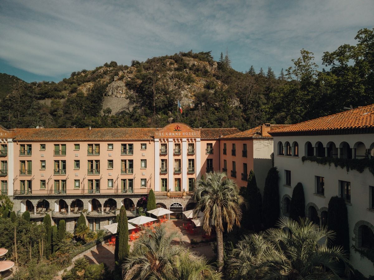 Un hotel con un patio central, varios pisos y un telón de fondo montañoso.