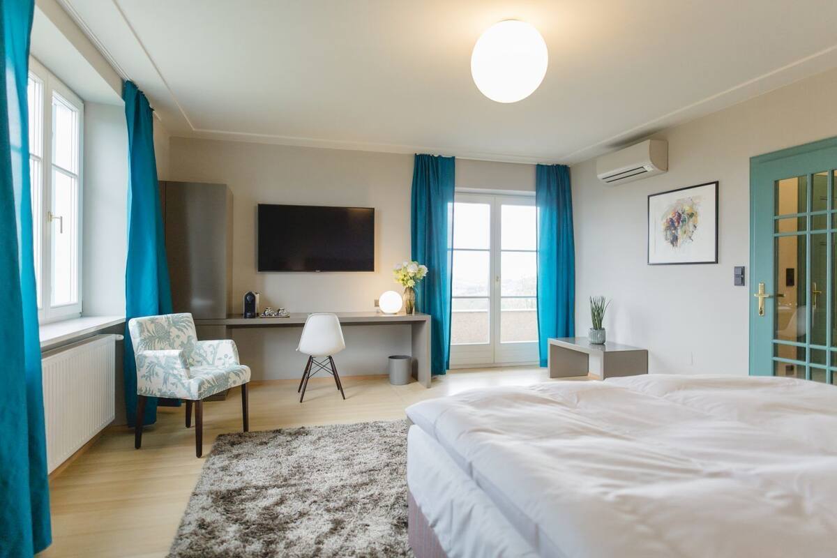 A modern hotel room with a large bed, a desk with a chair, a flat-screen TV, and a view of the outdoors.