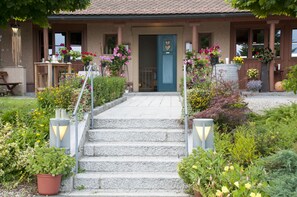 A building with a front entrance, steps leading up to it, and a variety of potted plants and flowers around the entrance area.