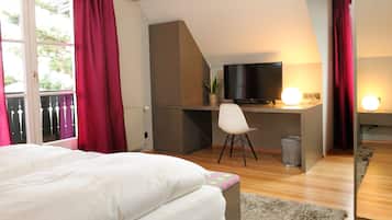 A bedroom with a bed, a desk with a chair, a television, and a window with curtains.