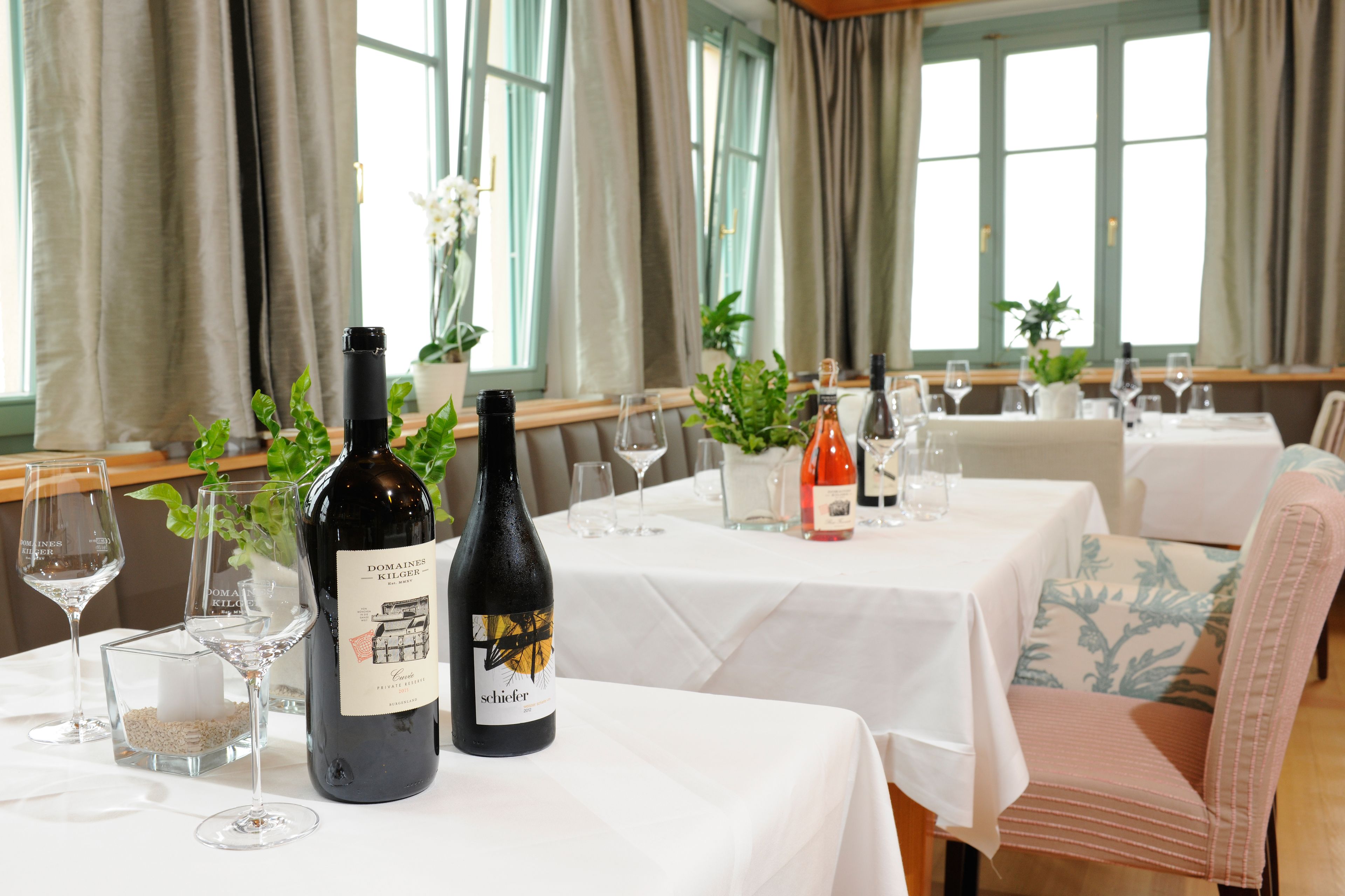 Uma sala de jantar com mesas preparadas para refeição, com garrafas e copos de vinho.