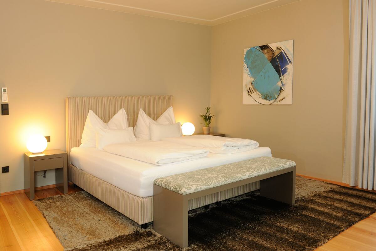 A neatly made bed with white linens, a bedside lamp, and a small bedside table.