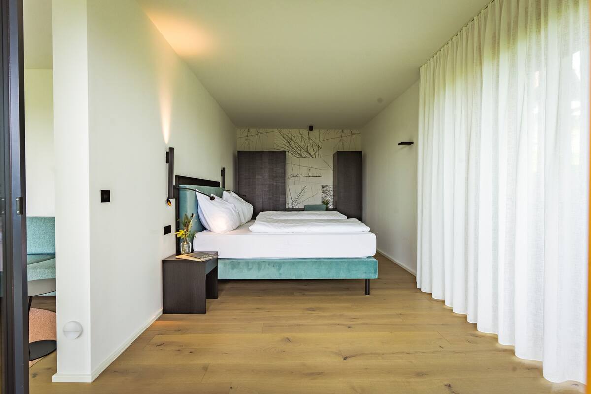 A bedroom with a bed, bedside tables, a nightstand, a wall-mounted lamp, and a curtain.