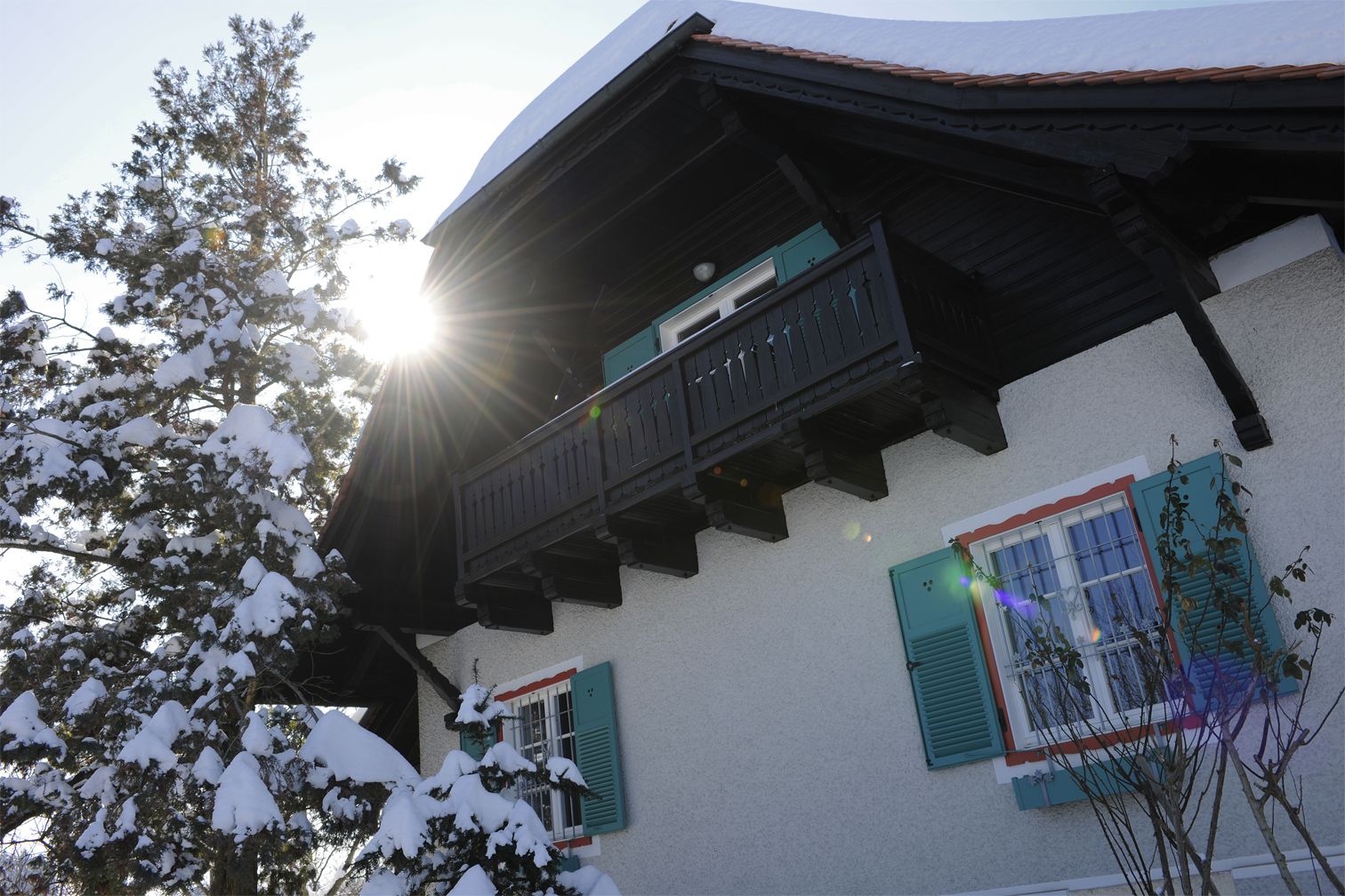 A building with a balcony, snow-covered trees, and a sun shining through the windows.