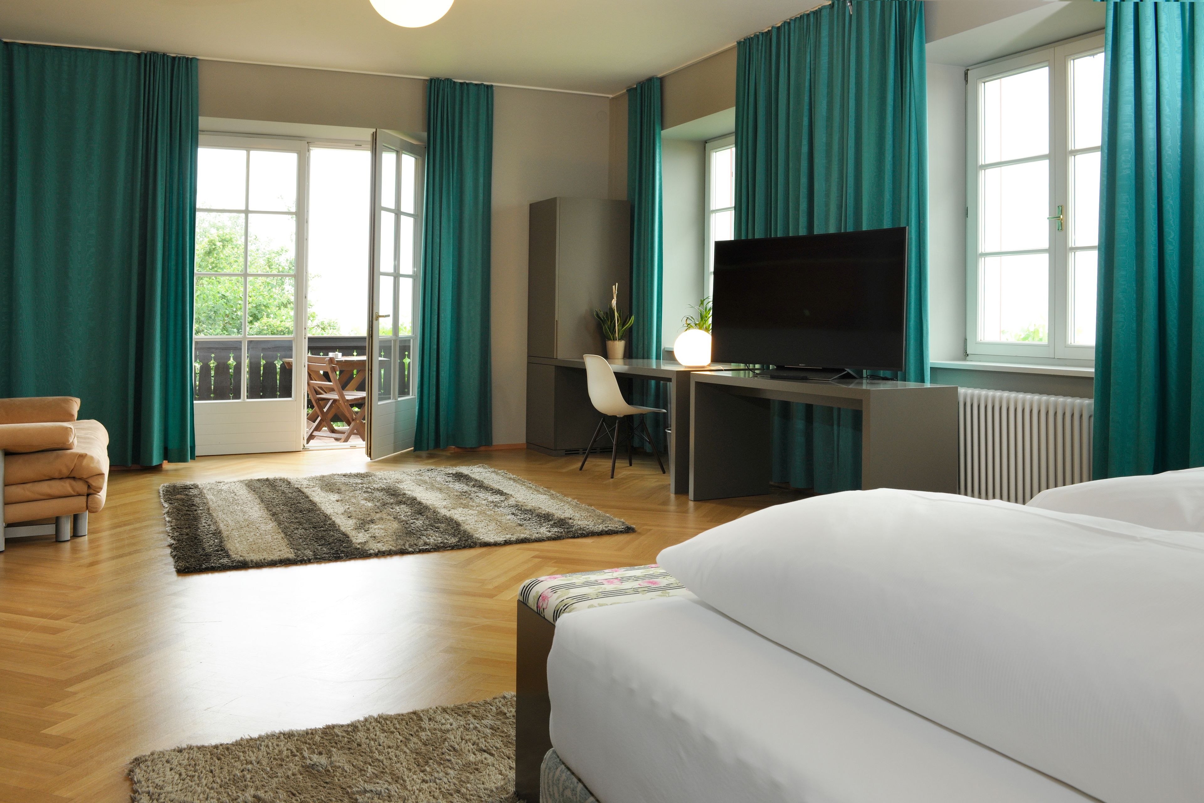 A hotel room with a bed, a desk with a TV, a chair, and a view of the outdoors.