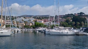 A marina with multiple sailboats docked, surrounded by buildings and greenery.