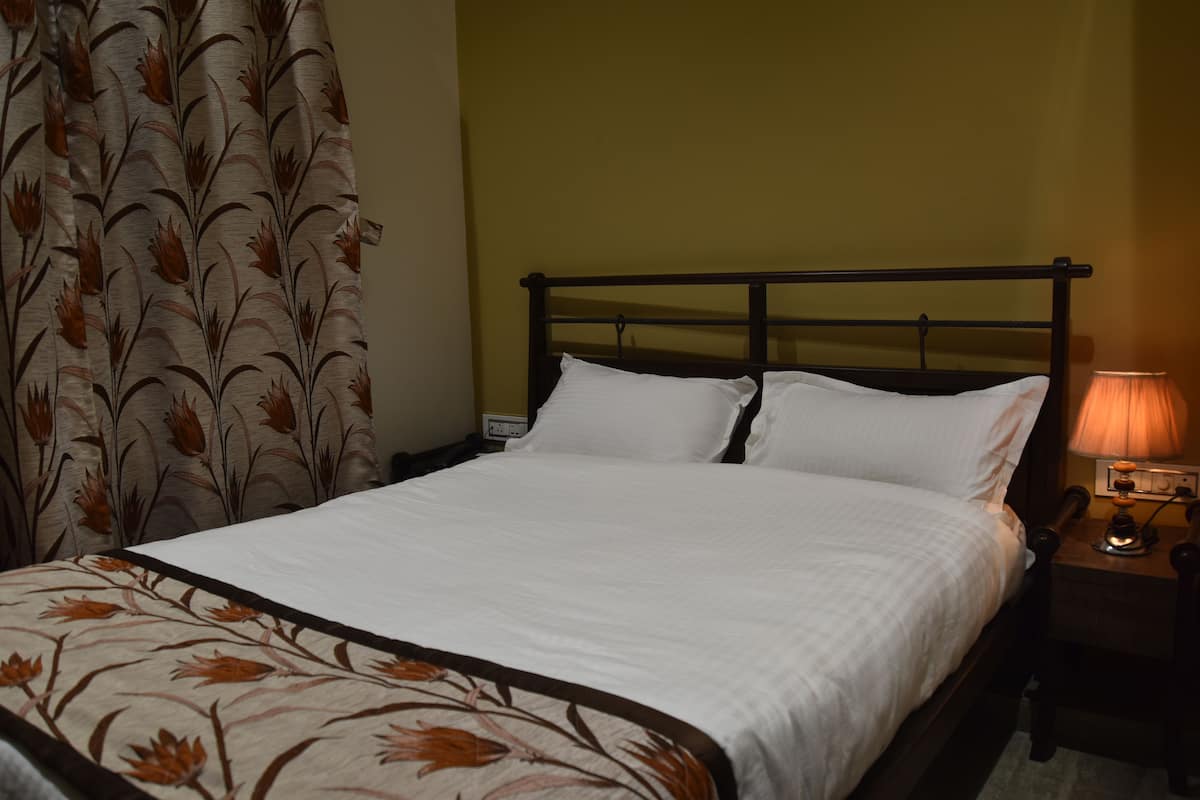 Uma cama bem arrumada com lençóis brancos, cabeceira de madeira e mesa de cabeceira com abajur.