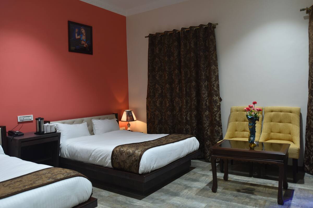 Quarto de hotel com duas camas, mesa de cabeceira, luminária, um vaso com flores e uma cadeira.