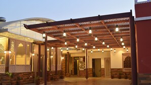 Un patio interior con una pérgola de madera, plantas en macetas y una estructura de vidrio al fondo.