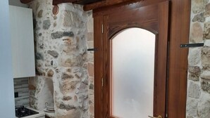 A kitchen with a stone wall, a wooden door with a frosted glass panel, and a white cabinet. - Residenza Cardinale (Tropea)