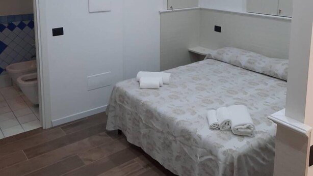 A bedroom with a bed, a bedside table, a mirror, and a wooden ceiling beam. - Residenza Cardinale (Tropea)