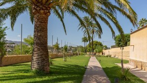 A pathway lined with palm trees and a well-maintained lawn, leading to a building with a stone facade. - Villa Benimarco by Costa CarpeDiem (Teulada)