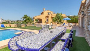 A poolside area with a tiled table and chairs, a pool, and a building with a yellow facade. - Villa Benimarco by Costa CarpeDiem (Teulada)