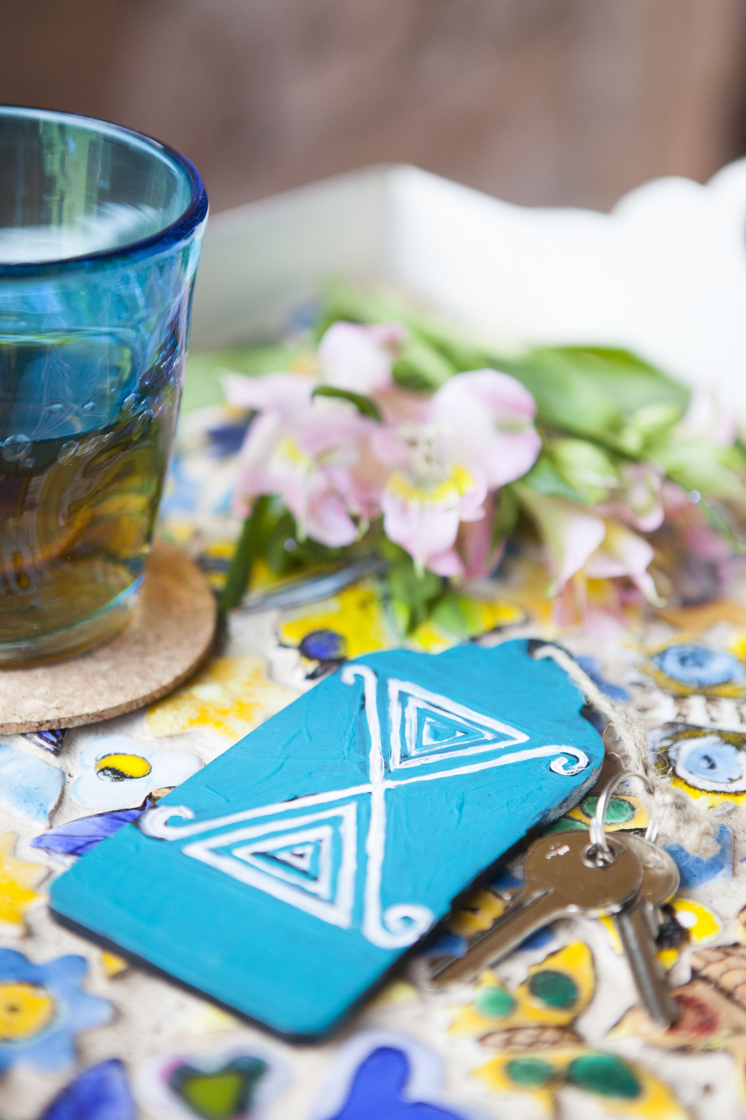 A blue glass cup, a blue card with white designs, and keys on a colorful surface with flowers.