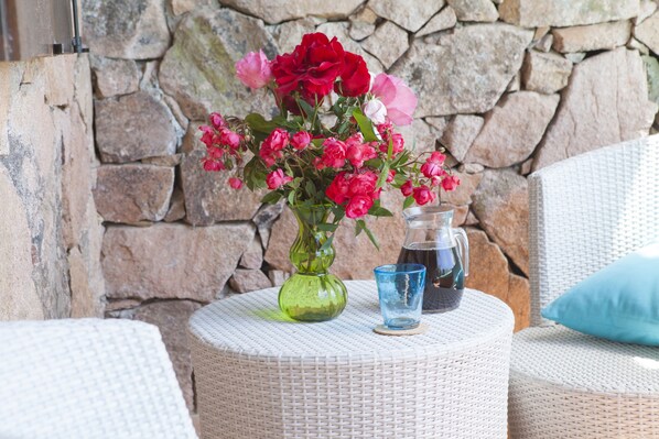 A wicker table with a vase of flowers, a glass, and a pitcher. - Residence Approdo Verde (San Teodoro)