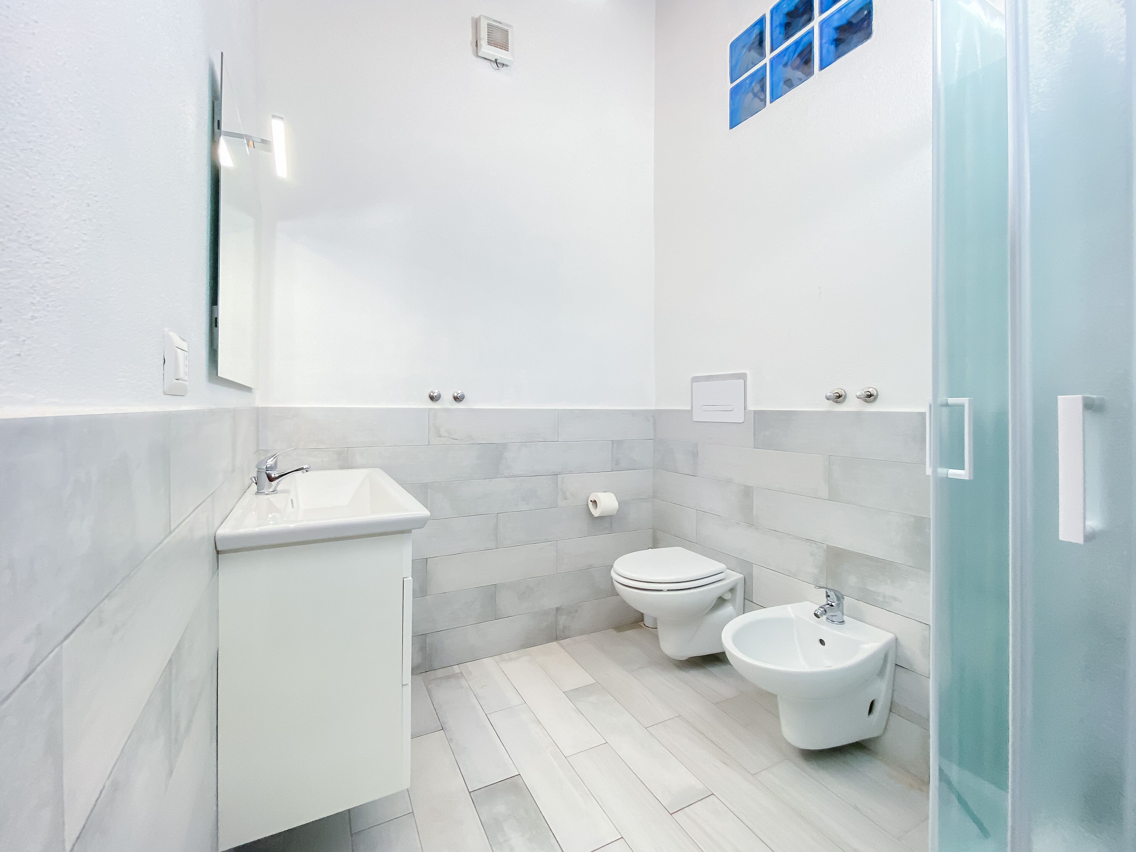 A modern bathroom with a white sink, toilet, bidet, and a glass shower enclosure.