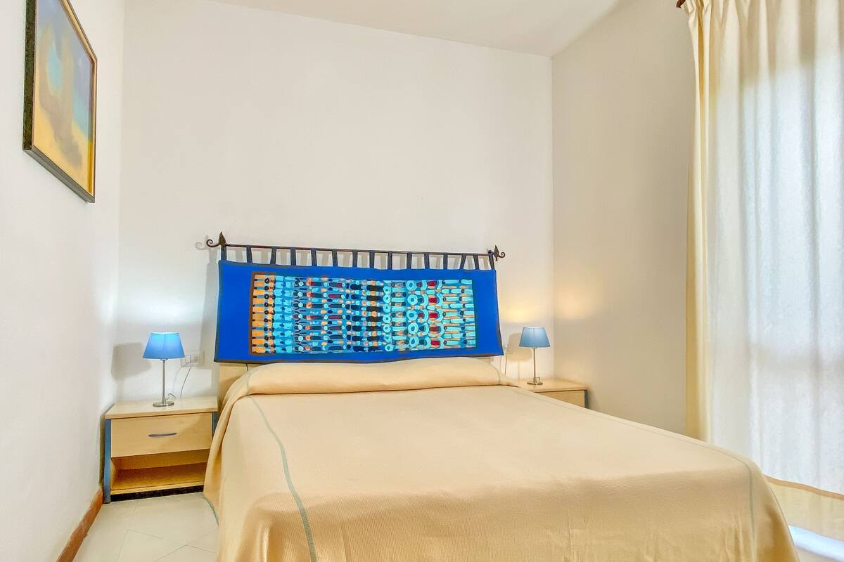 Ein ordentlich eingerichtetes Schlafzimmer mit einem Bett, zwei Nachttischen, einem Wandbild und einer Ablagefläche.