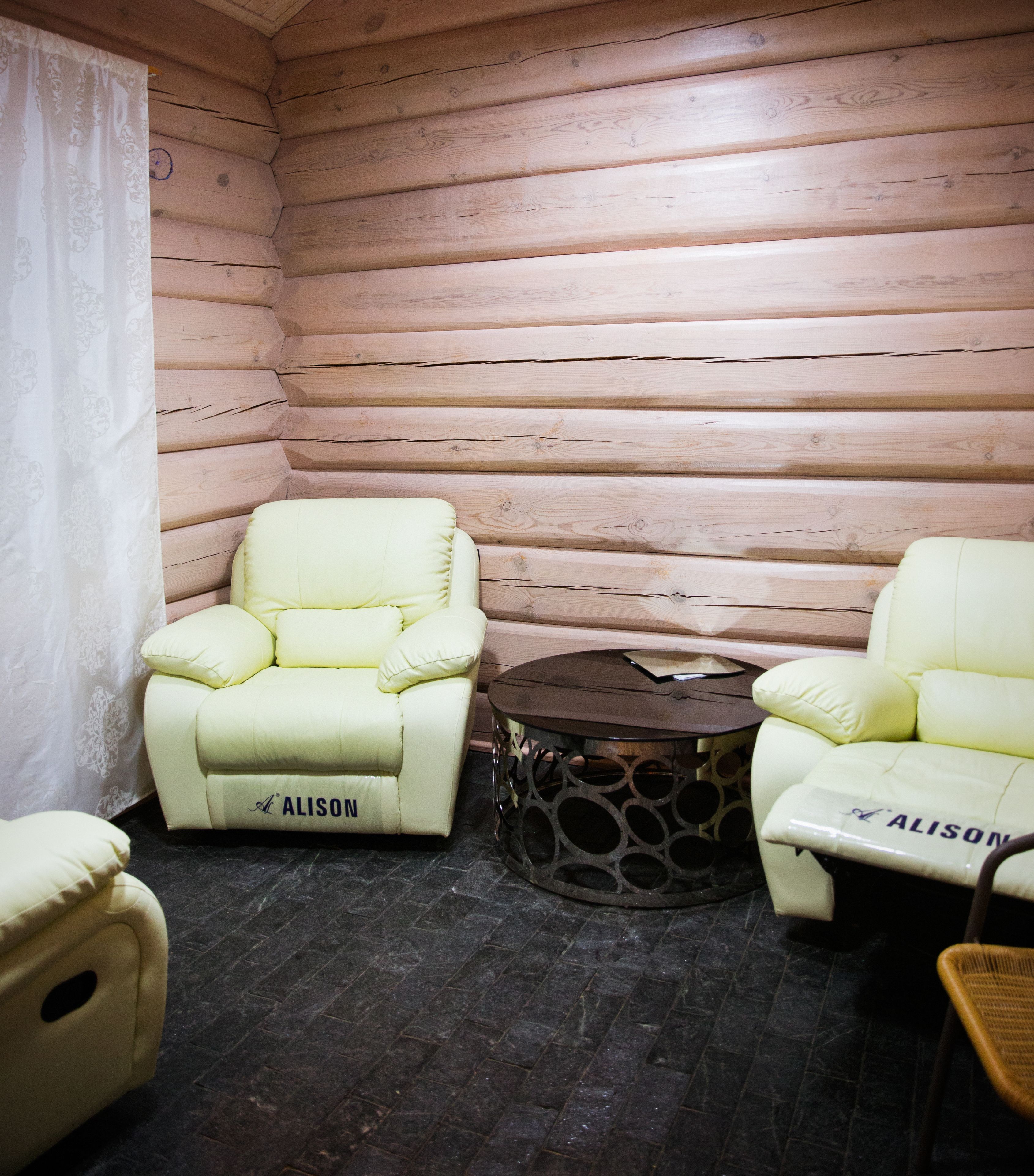 A log cabin room with two cream-colored chairs labeled 'ALISON' and a small round table with a dark top.