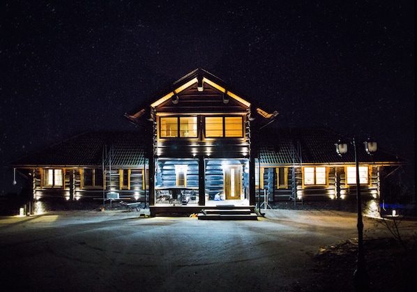 A log cabin with a porch and multiple windows, surrounded by a snowy landscape.