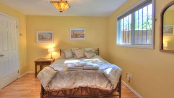 Un dormitorio con cama, mesita de noche, lámpara, ventana con barrotes y dos cuadros en la pared.