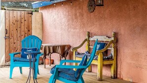Eine Terrassenfläche mit zwei türkisfarbenen Stühlen, einem kleinen Tisch, einer Holzbank und einer rustikalen Wand.
