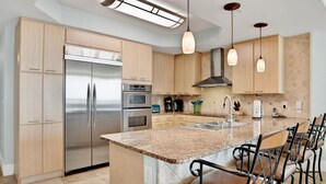 Una cocina moderna con una isla grande, electrodomésticos de acero inoxidable e iluminación colgante.