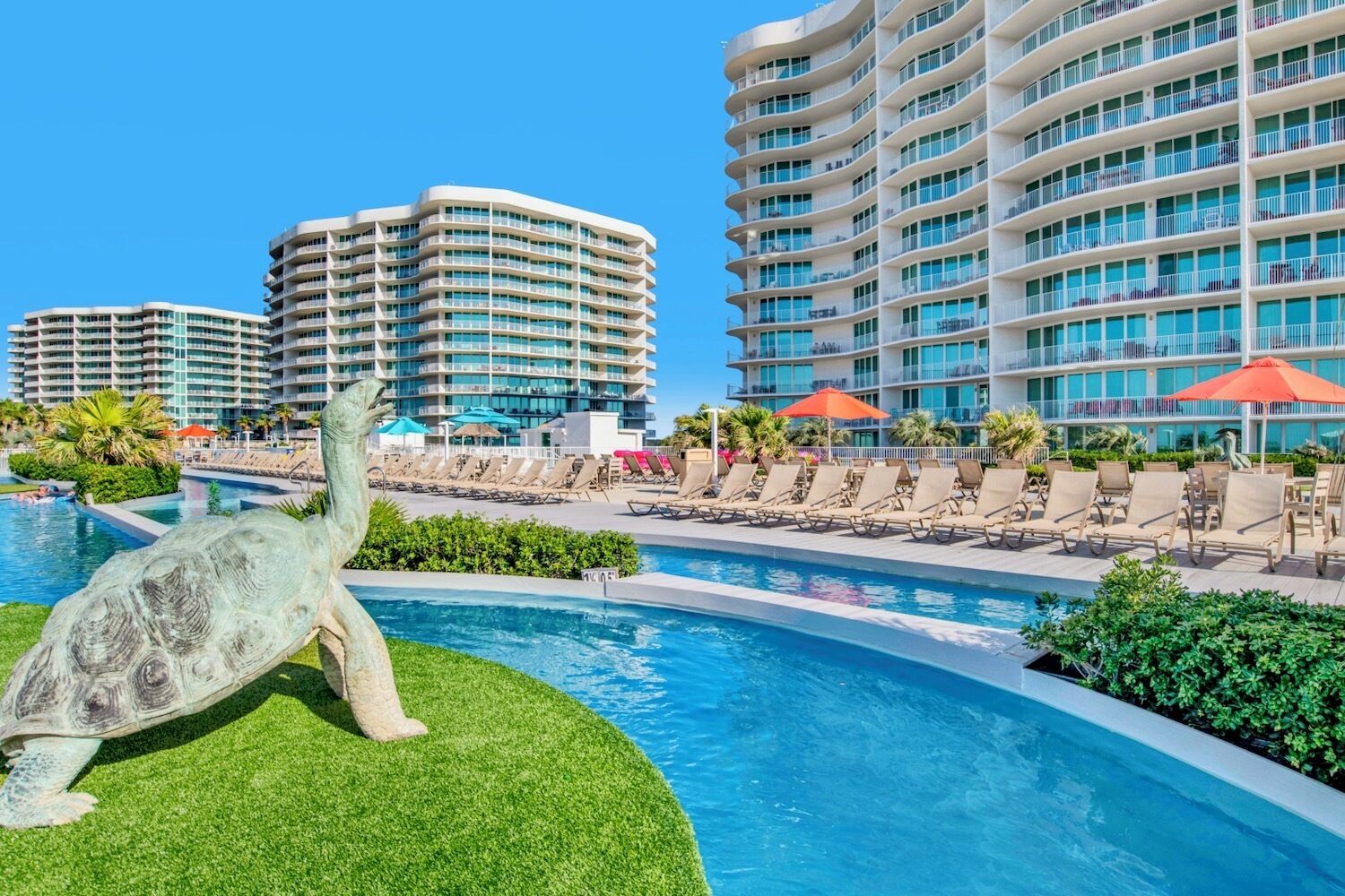 Un complex turístic amb una piscina gran, gandules i una estàtua de tortuga.