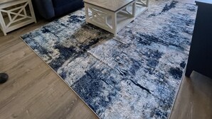 Una sala de estar con dos sofás azul oscuro, una mesa de centro blanca y un tapete estampado.