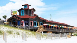Un edificio de madera con techo rojo y puertas coloridas, situado en una playa de arena.
