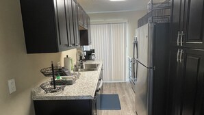 Cocina compacta con armarios oscuros, un refrigerador de acero inoxidable y una encimera con fregadero.