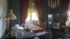 Un dormitorio clásico con cama con dosel, candelabro y cortinas rojas.