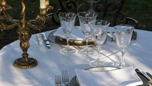 Una mesa lista para una comida al aire libre, con un candelabro, copas de vino y cubiertos.