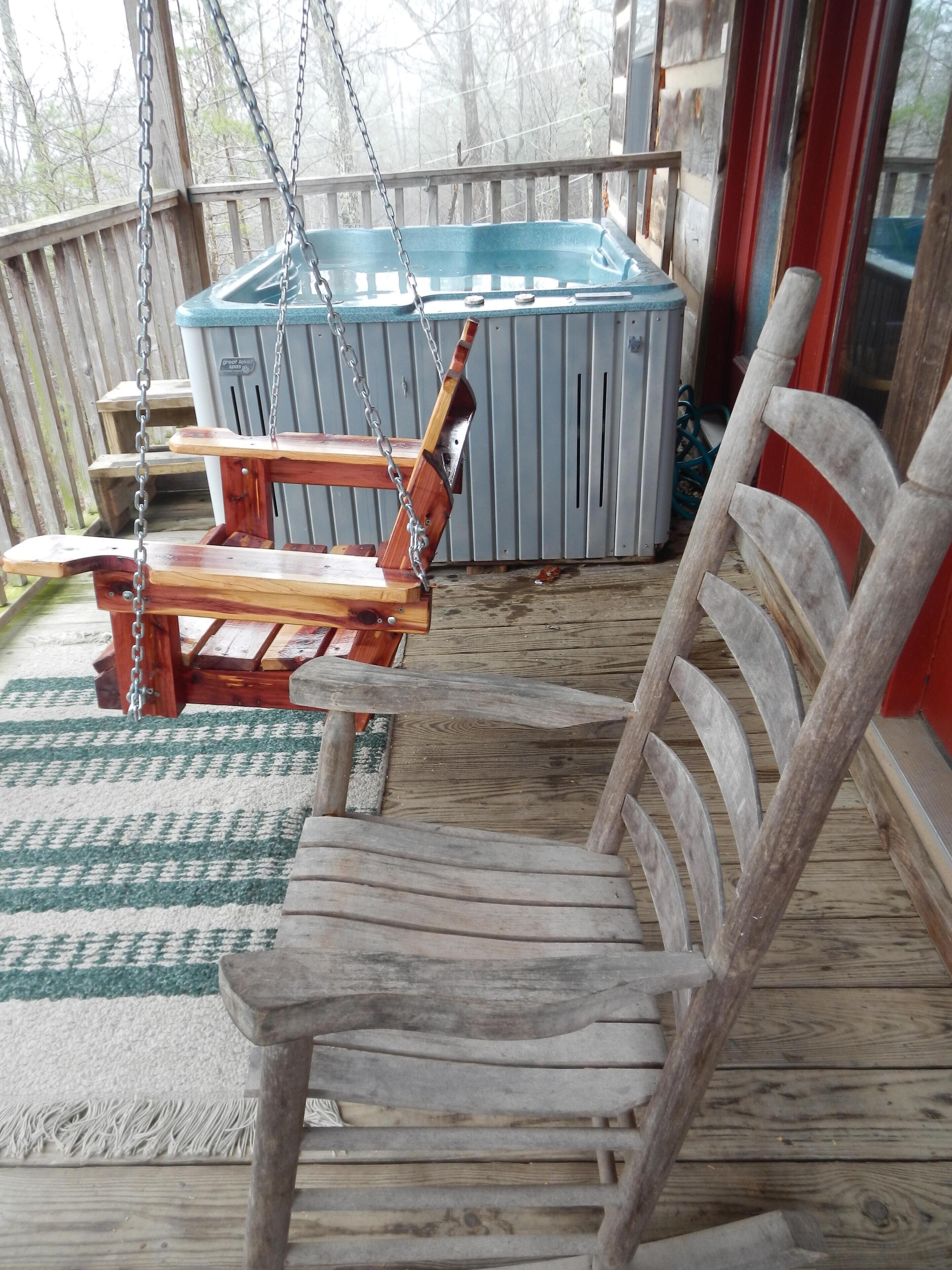A wooden swing chair on a wooden deck with a hot tub in the background.