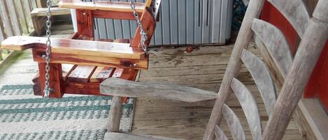 A wooden swing chair on a wooden deck with a hot tub in the background.