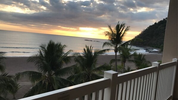 A balcony with a view of the beach and ocean during sunset.