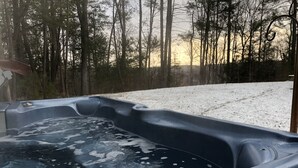 A hot tub with a partially frozen surface, surrounded by a snowy landscape and trees.