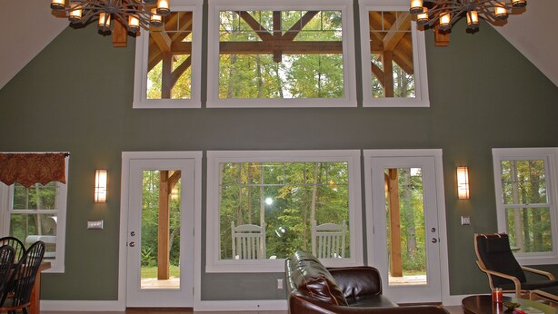 A spacious room with a high ceiling, large windows, and a wooden ceiling structure. There is a leather sofa and a dining table with chairs.